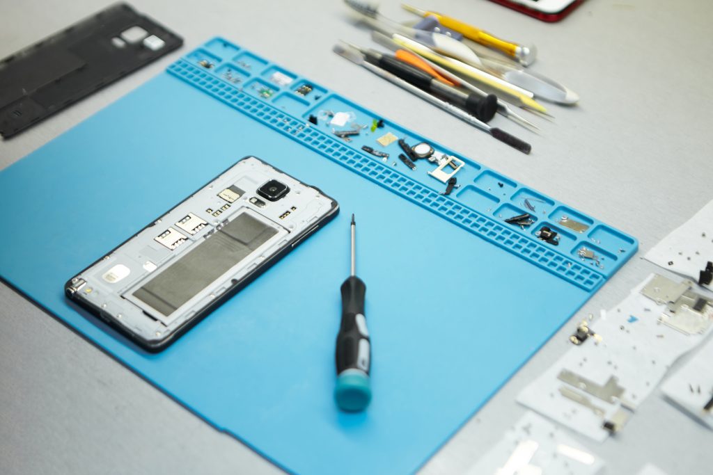plan rapproché du plan de travail d'un réparateur téléphone avec outils spéciaux posés à côté d'un smartphone démonté